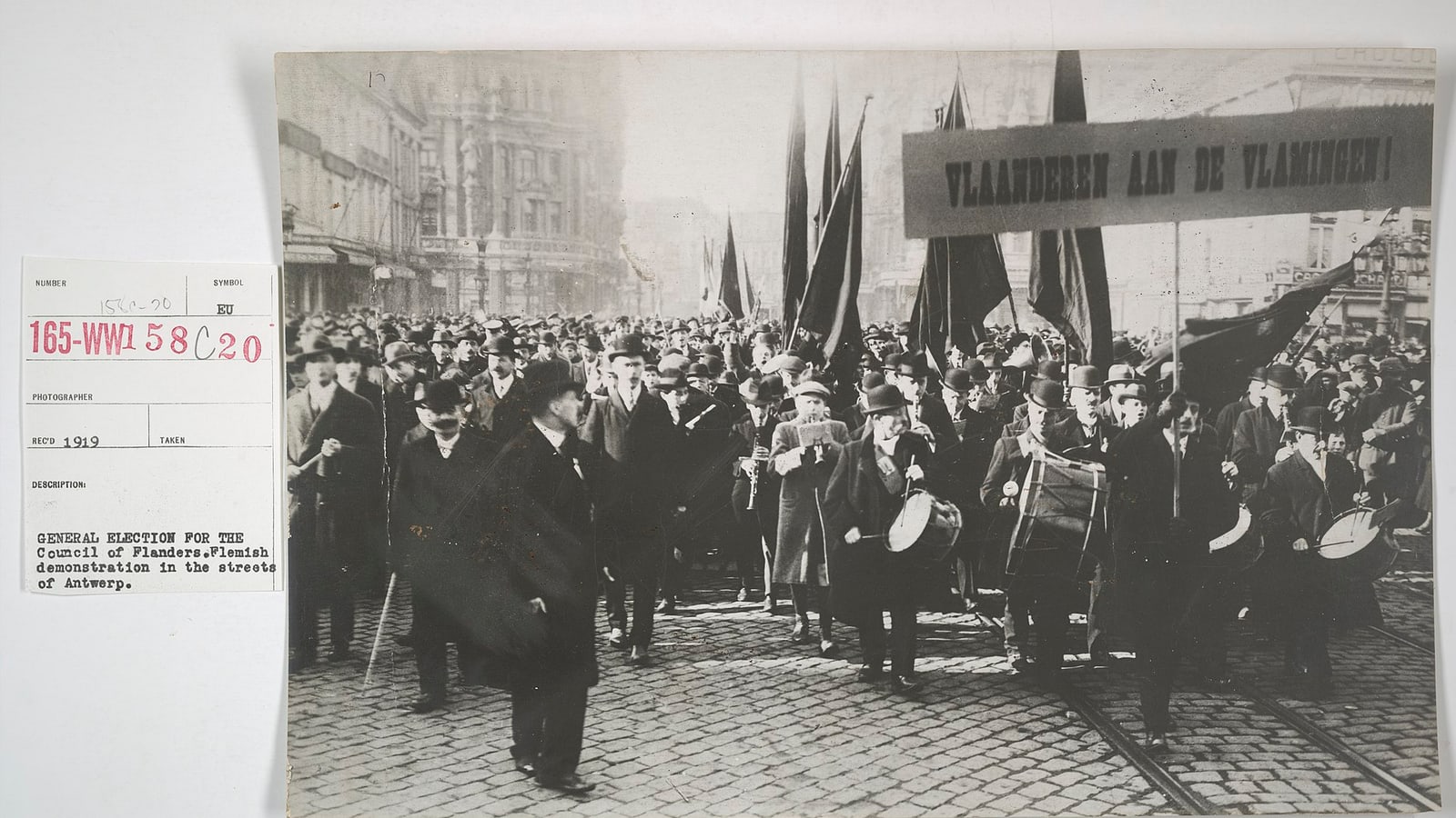 A large crowd marches down a cobblestone street in antwerp during a flemish demonstration, with drummers and flags visible — illustrative photograph