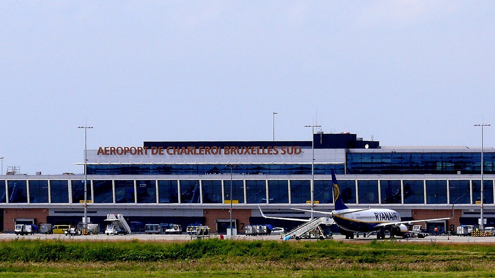A modern airport terminal with a ryanair plane parked at the gate under clear skies — illustrative photograph