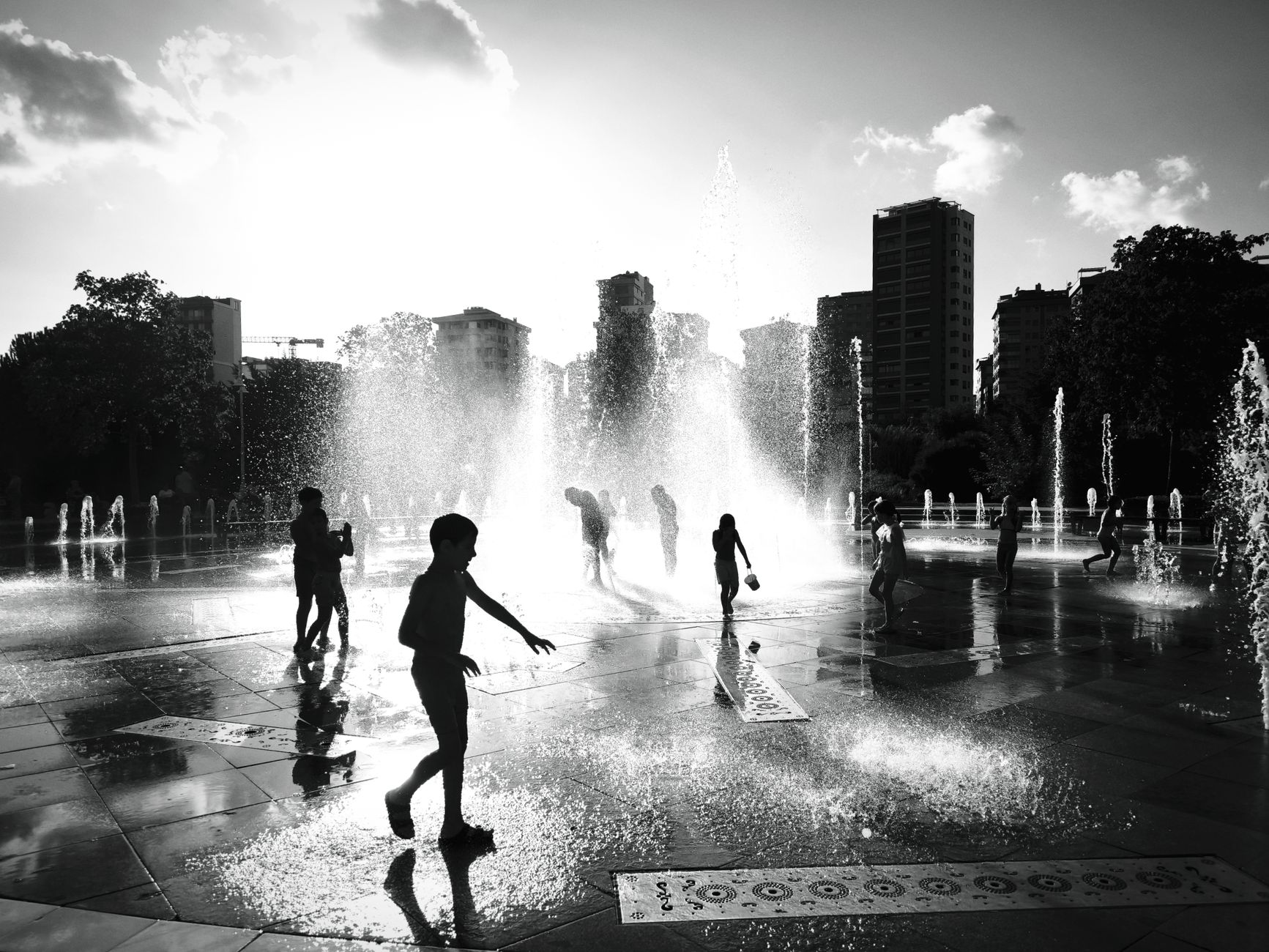 Image illustrating: People cooling off in an urban park fountain during a summer heatwave (editorial)